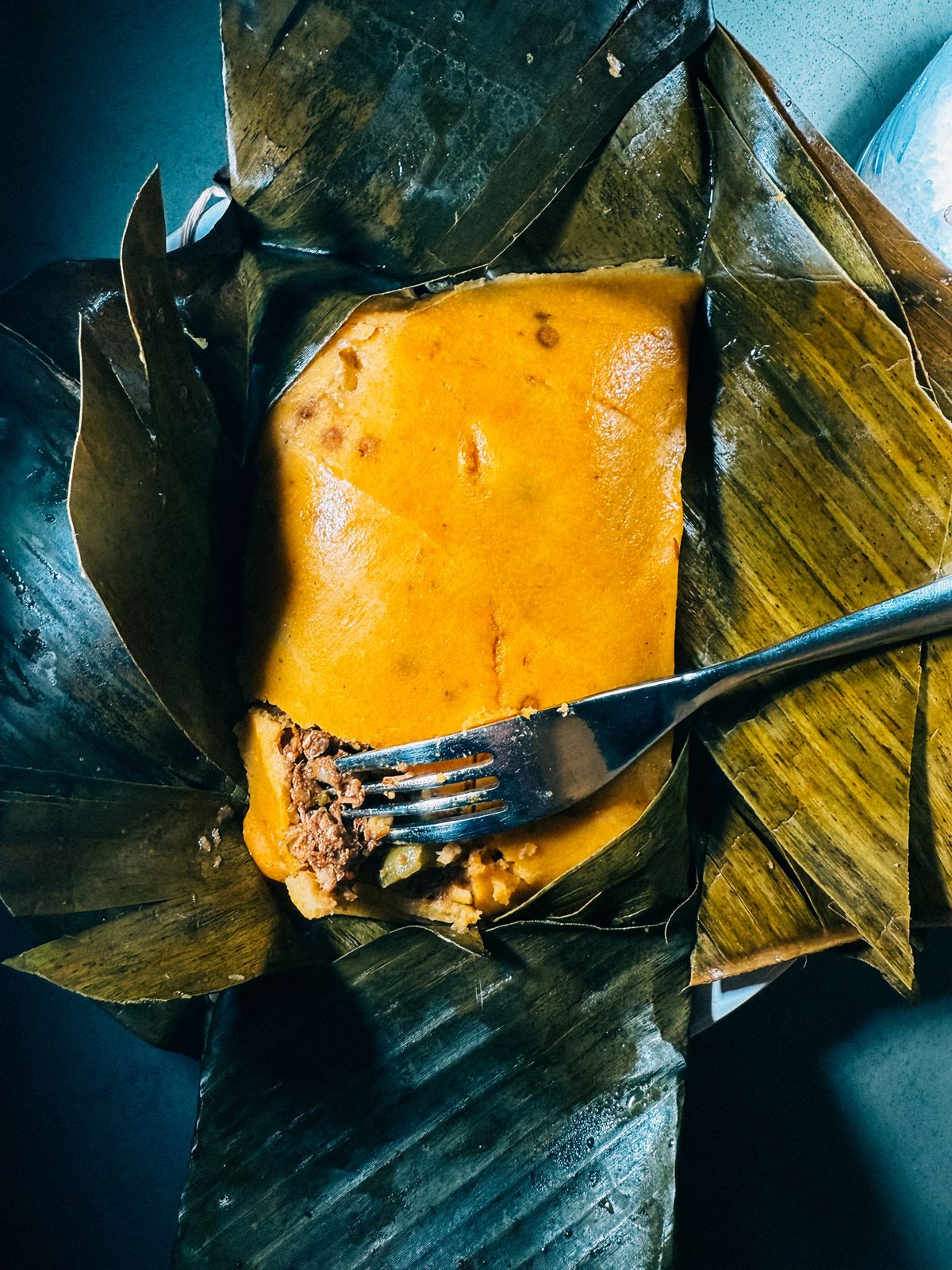 Tamal valluno abierto, masa de maíz sazonada con hogao y relleno de carne, envuelto en hoja de plátano
